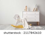 Small photo of Rocking horse with plaid and chest of drawers near light wall