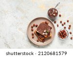 Small photo of Plate of bread with chocolate paste and hazelnuts on light background