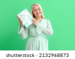 Fashionable mature woman holding gift box on green background. International Women's Day celebration