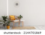 Comfortable armchair, houseplants and table near white wall