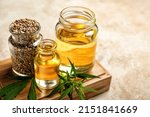 Board with bottles of hemp oil and seeds on light background, closeup