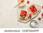 Board with sugar powdered puff pastry, strawberry and honey on light background