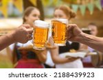 Small photo of Men clinking mugs with beer during celebration of Octoberfest outdoors