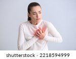 Small photo of Young woman having heart attack on light background