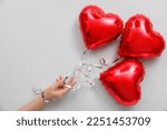 Female hand with red heart shaped balloons on light background. Valentine's Day celebration