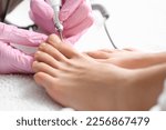Small photo of Young woman getting pedicure with milling cutter in beauty salon, closeup