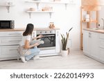 Young woman opening electric oven in kitchen