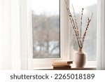 Vase with pussy willow branches and books on windowsill in room
