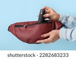 Woman putting pepper spray in bag on blue background