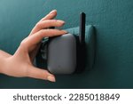 Small photo of Woman plugging black WiFi repeater in electric socket on green wall