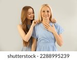 Small photo of Young woman putting necklace around her mother's neck on grey background