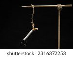 Small photo of Cigarette hanging on gallows against dark background. Stop smoking concept