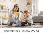 Nanny with little boy blowing soap bubbles at home