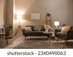 Interior of living room with cozy grey sofa, armchair and glowing lamps