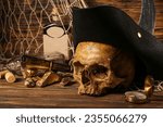 Small photo of Human skull with pirate hat, golden nuggets, bottle of rum and travel equipment on brown wooden background