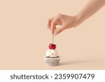 Woman decorating tasty cupcake with cherry on beige background