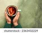 Woman holding cup of hot mulled wine with apple and pomegranate on grunge background