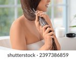 Young brunette woman applying hair product in bathroom, closeup