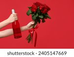 Female hands holding bottle of wine and roses on red background. Valentine's Day celebration