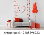 Interior of festive living room with grey sofa, heart-shaped balloons and decorative hearts. Valentine's Day celebration