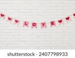 Bunting with word LOVE hanging on white brick wall. Valentine's Day celebration