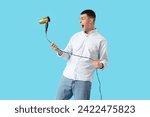 Playful young man with hair dryer on blue background