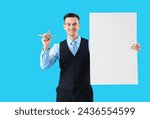 Small photo of Handsome steward with blank poster and wooden airplane on blue background