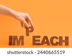 Small photo of Female hand with wooden letters spelling word IMPEACHMENT on orange background