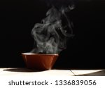 bowl of hot soup with steaming on wooden table on black background
