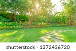 Green grass lawn in a garden with random pattern of grey concrete steping stone , Flowering plant, shurb and trees on backyard under morning sunshine with good care landscapes in a pubblic park  