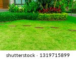 Smooth fresh green grass lawn with random pattern walkway of brown laterite steping stone in a garden of flowering plant,  shurb and trees on backyard in front the house
