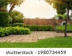Back and front yard cottage garden, flowering plant and green grass lawn, brown pavement and orange brick wall, evergreen trees on background, in good care maintenance landscaping in park 