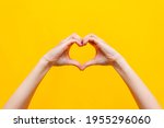 Female hands showing a heart shape isolated on a bright
color yellow background. Sign of love, harmony, gratitude, charity. Feelings and emotions concept
