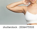 Small photo of Cropped shot of a young woman with excess fat on her upper arm with marks for liposuction or plastic surgery isolated on a gray background. The loose and saggy muscles. Overweight