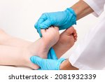 Small photo of Examination of a child by an orthopedist. Close-up of female doctor's hands in blue medical gloves holding a kid's foot. Pathology of bone structures, flat feet, injury. Foot treatment