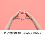 Female hands showing a heart shape isolated on a color light pink background. Sign of love, harmony, gratitude, charity. Feelings and emotions concept