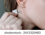 A young woman applying a temporary mini tattoo in the form of a heart and a cardiogram on her neck