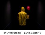 Hooded yellow figure with red balloon in dark creepy corridor