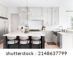 Small photo of CHICAGO, IL, USA - FEBRUARY 28, 2021: A luxurious kitchen with a large island, gold faucet and sputnik chandelier, stainless steel appliances, and white marble countertops.