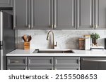 A kitchen sink detail shot with grey cabinets, a white marble countertop and backsplash, and decorations.