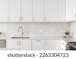A beautiful kitchen faucet detail with white cabinets, a gold faucet, white marble countertops, and a brown picket ceramic tile backsplash.
