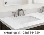 Small photo of A bathroom faucet detail with a bronze widespread faucet, white marble countertop, and a dark wood cabinet.