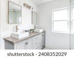 Small photo of An elegant, renovated bathroom with white sinks, grey vanity, granite countertop, and bronze hardware, faucets and light.