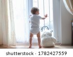 Small photo of Backside of little baby boy standing on tiptoes next to window home with teddy bear looking outside during coronavirus,Covid-19 outbreak quarantine,social distancing.Emotional kid feeling lonely alone