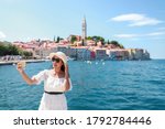 Young Asian tourist woman taking picture or selfie at Harbour rovinj city, Croatia by smartphone. Happy freedom girl traveling in Europe in summer time with copy space for text.