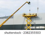 Small photo of Sandwich panels wall assembly using telescopic boom crane and yellow self propelled scissor lift platform