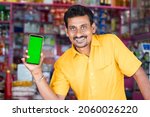 Smiling Merchant at groceries store hold mobile with green screen mock up by looking at camera - concept of Technology, advertisement, online booking and e-commerce.