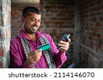 Small photo of young indian daily wager making online payment using credit card on mobile phone at workplace - concept of technology, finance, online shoping and using digital payment.