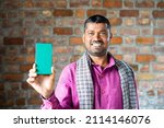 Small photo of rack focus shot of indian daily wager showing green screen mobile phone by looking at camera - concept of technology, blue collar job, advertisment and promotion.