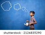 Small photo of poor tea selling kid thinking by holding tea glass and container in hand with cloud doodle drawing on blue background - cocept of poverty, child labour and imagination